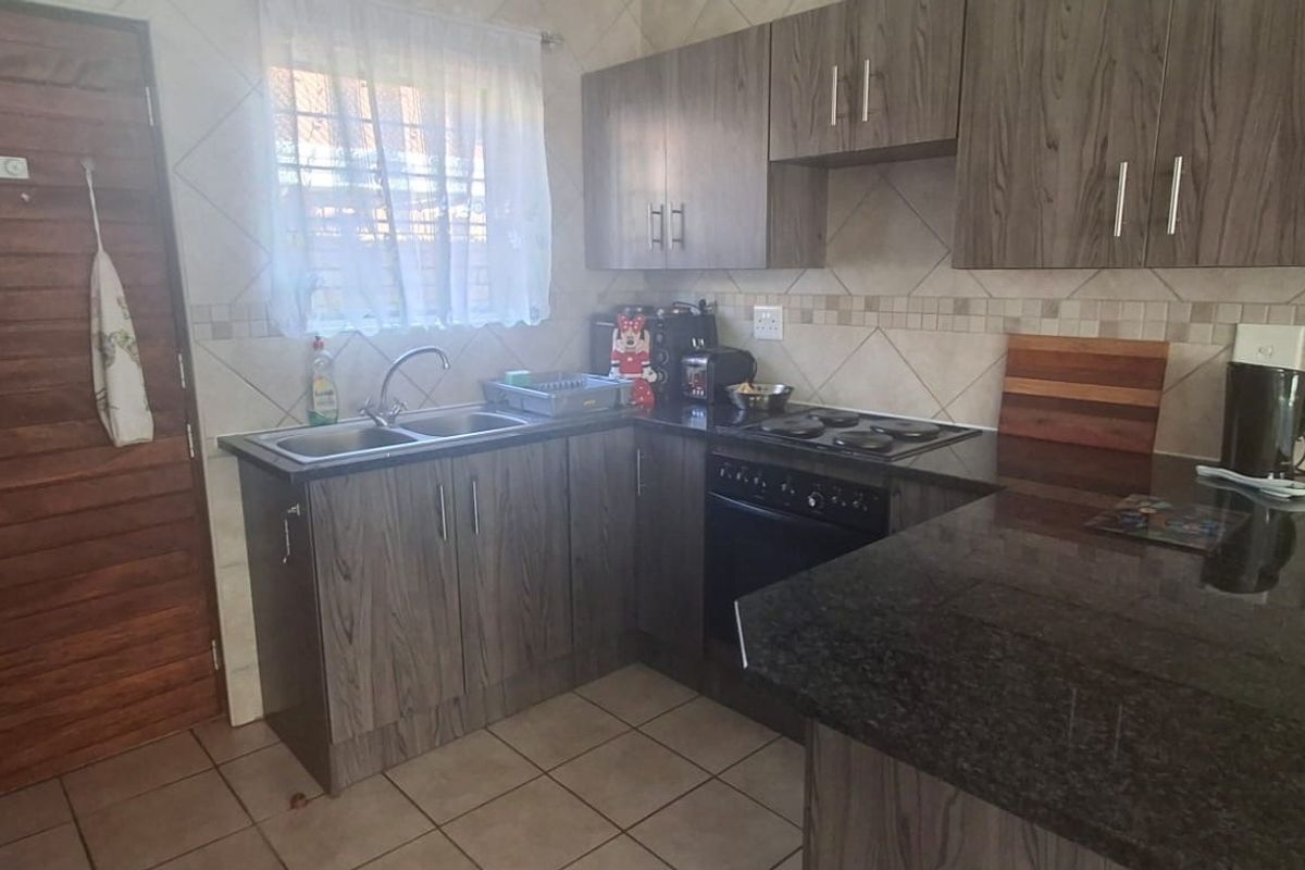A functional kitchen featuring dark wood-look cabinetry, granite countertops, a built-in electric hob and oven, and tiled flooring.