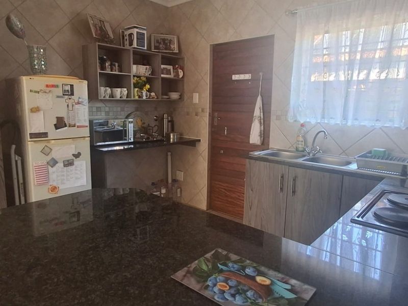 Functional kitchen featuring granite countertops, double bowl sink, built-in cabinetry, and an electric hob with tiled splashback finishes.
