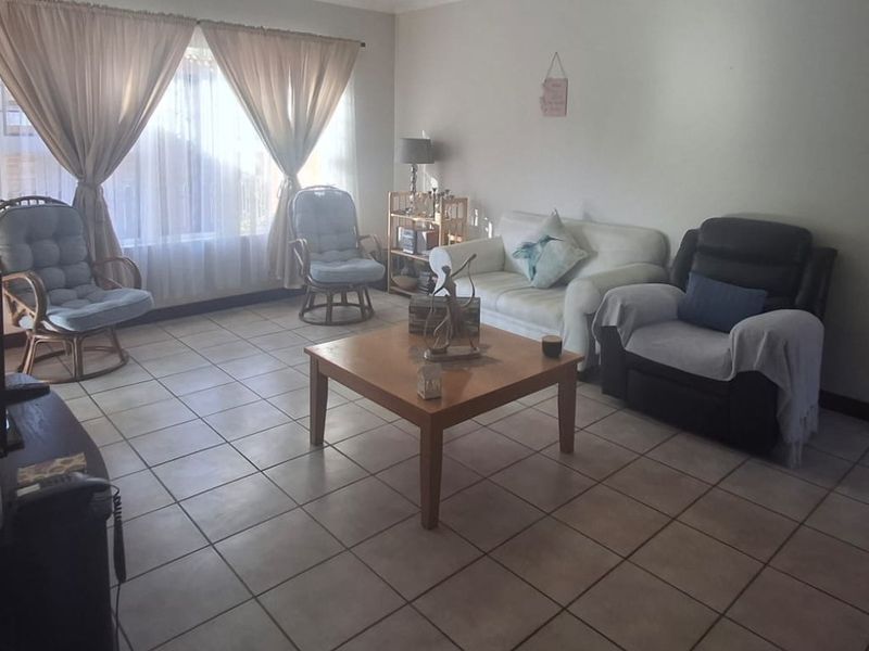 A spacious living room featuring neutral ceramic floor tiles and large windows with curtain tracks, offering a functional and well-lit living space.