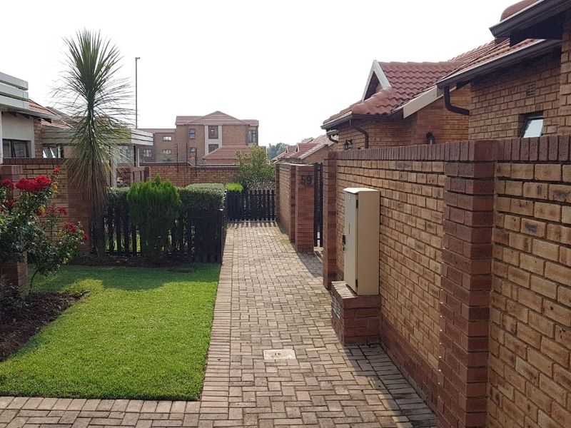 A well-maintained front entrance pathway featuring brick boundary walls, paved flooring, and established garden landscaping within a retirement village setting.