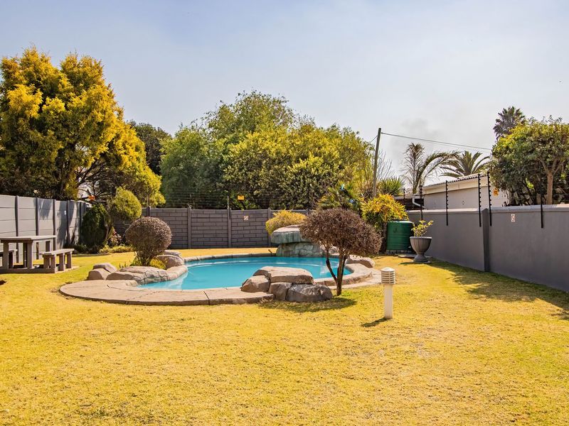 A well-maintained outdoor pool area featuring a rock-accented swimming pool, manicured lawn, and secure perimeter walling with electric fencing.