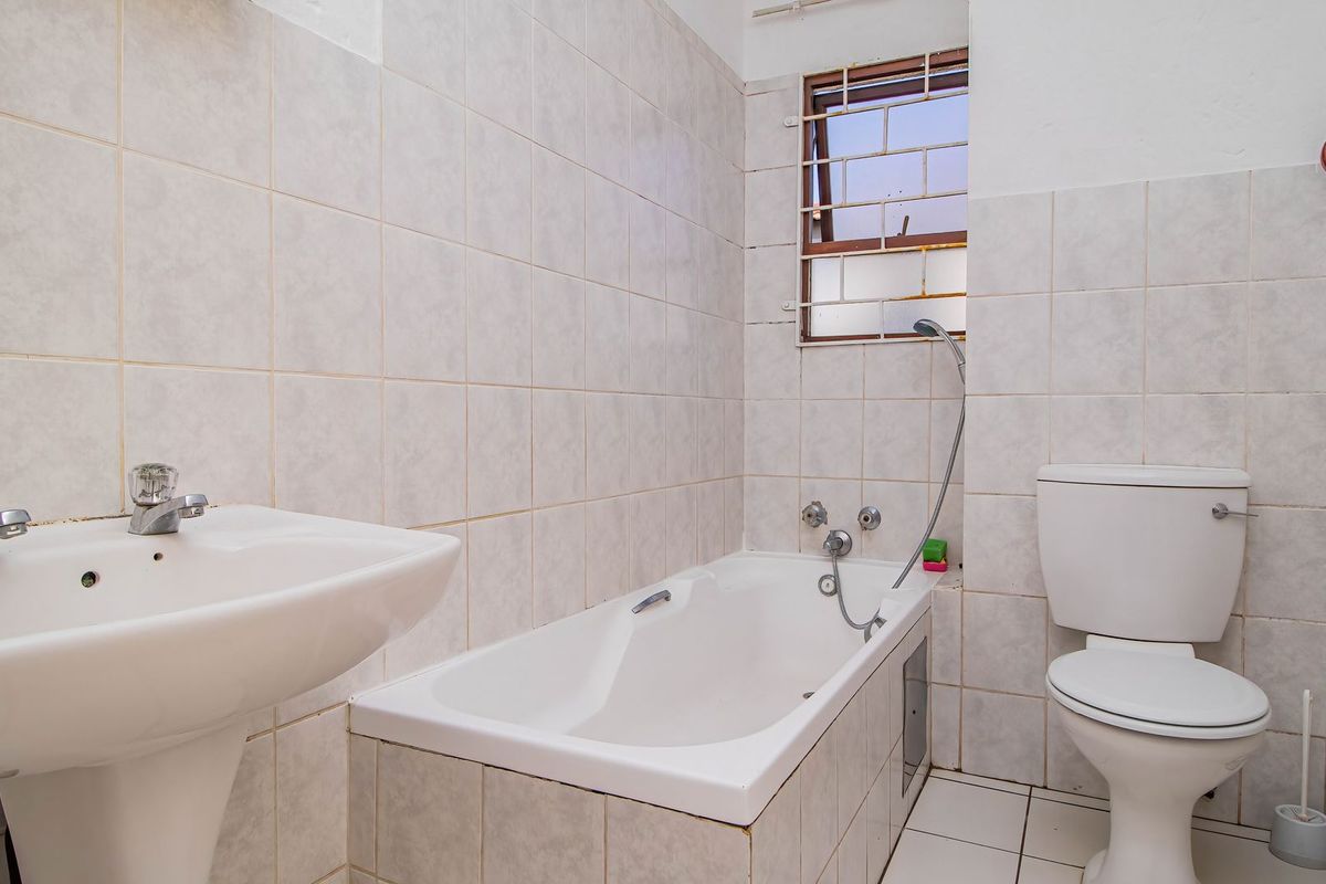 A functional bathroom featuring a pedestal basin, built-in bathtub with shower mixer, and a standard toilet, finished with neutral ceramic wall and floor tiles.