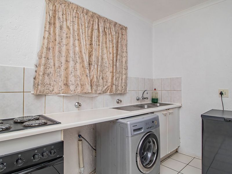 A functional kitchen area featuring a built-in stove, double sink, tiled backsplash, and base cabinetry with space for laundry appliances.
