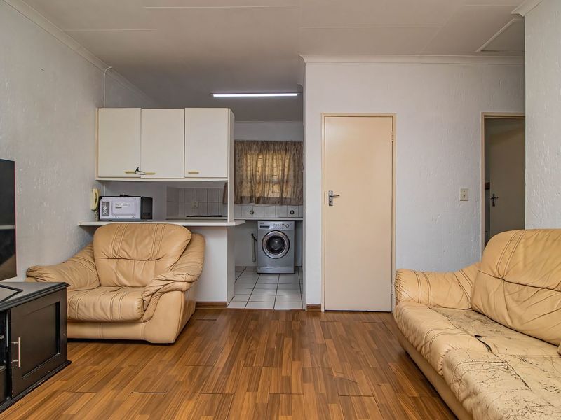 Open plan living area featuring laminate flooring, connected to a compact kitchen and laundry area with built-in cabinetry and tiled flooring.