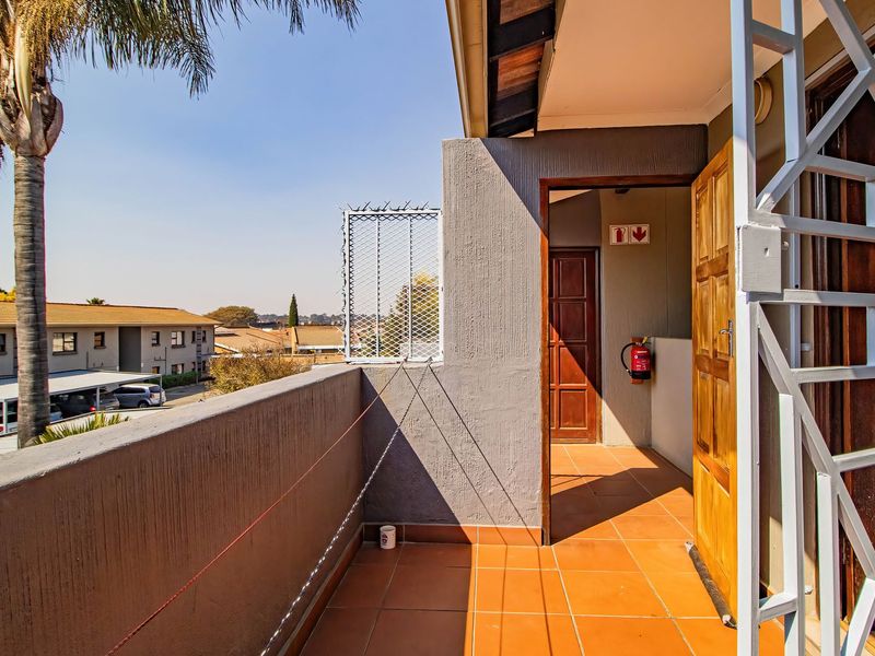 A private balcony featuring tiled flooring, a security gate, and a fire extinguisher, offering an elevated view of the surrounding apartment complex.