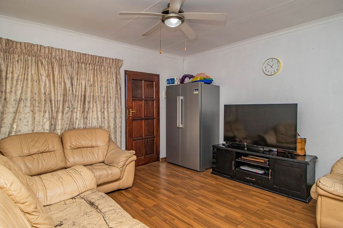 A living room featuring laminate flooring, a ceiling fan, and a timber door, providing a functional space with potential for cosmetic updates.