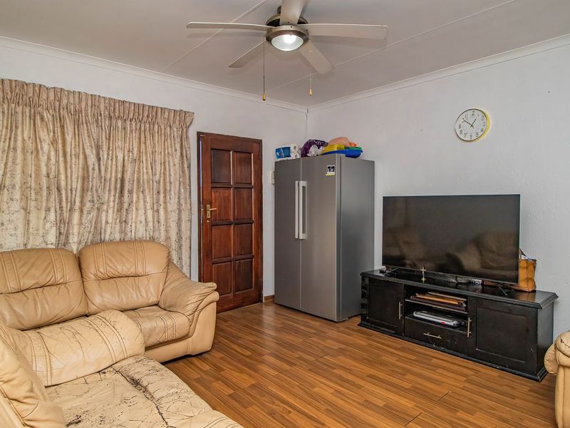 A living room featuring laminate flooring, a ceiling fan, and a timber door, providing a functional space with potential for cosmetic updates.