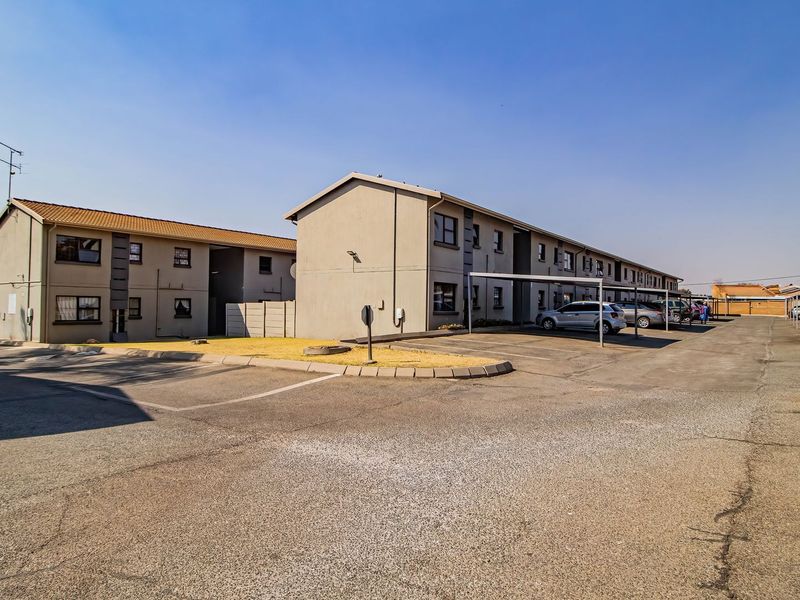 Exterior view of an apartment complex featuring paved parking areas, covered carports, and multi-story residential buildings with tiled roofing.