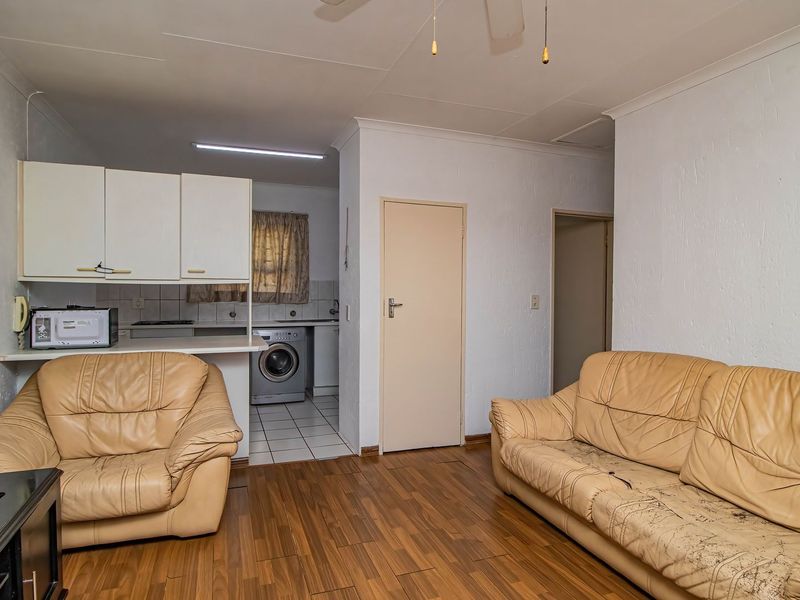 Open-plan living area featuring laminate flooring, connected to a functional kitchen with built-in cabinetry and laundry plumbing.