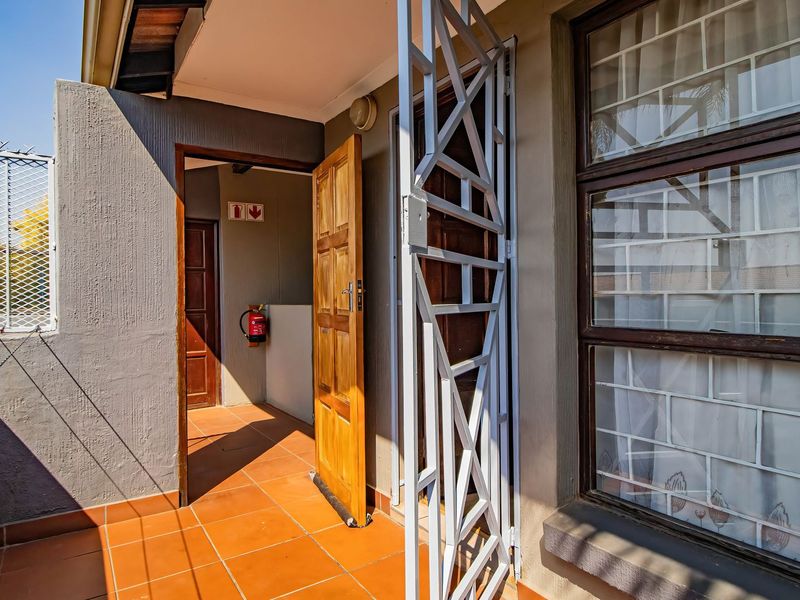 A covered balcony area featuring tiled flooring, a security gate, and a timber entrance door with external security bars on the windows.