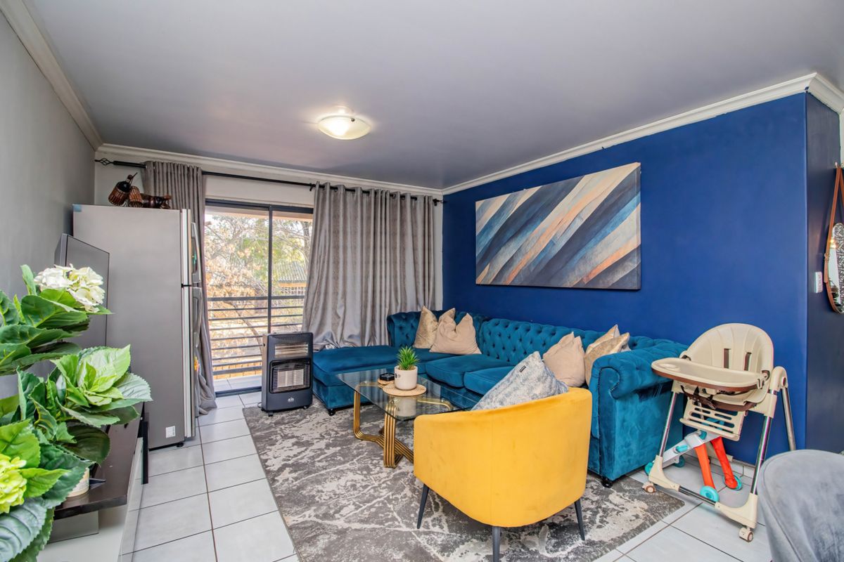 A well-maintained living room featuring tiled flooring, a bold blue accent wall, and a sliding glass door providing access to the balcony.