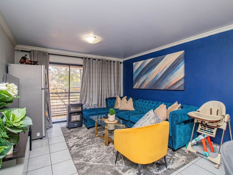 A well-maintained living room featuring tiled flooring, a bold blue accent wall, and a sliding glass door providing access to the balcony.