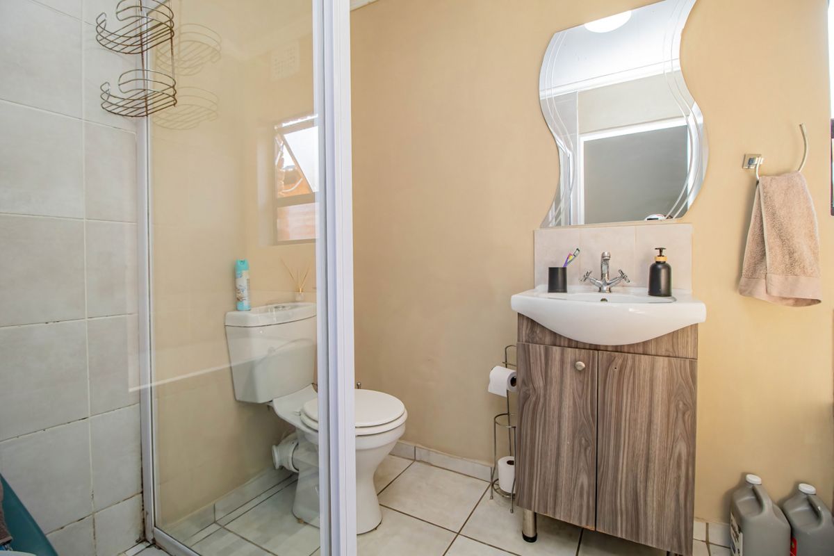 A functional bathroom featuring a glass-enclosed shower, a modern wood-finish vanity with a basin, and a standard toilet.
