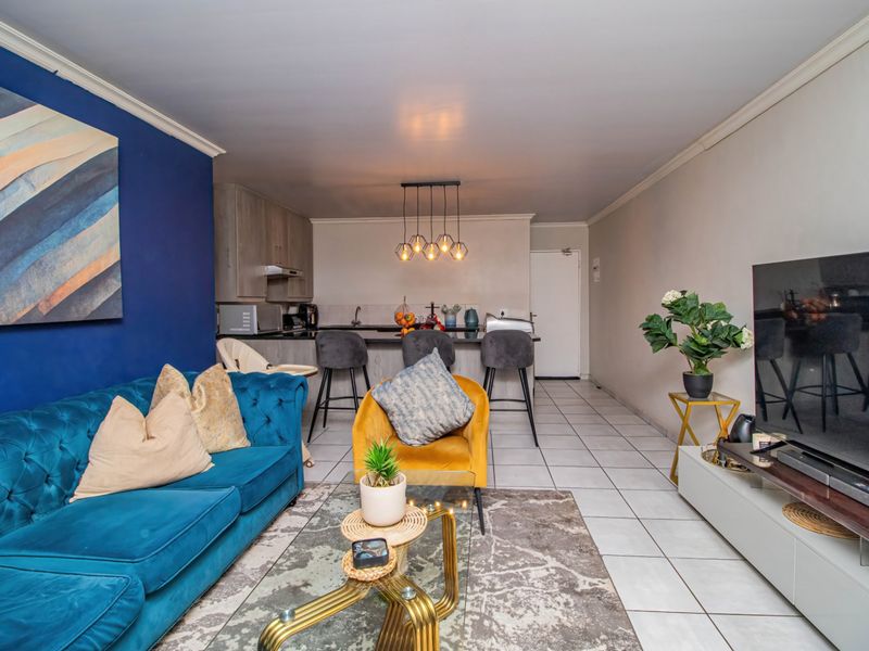 An open-plan living and kitchen area featuring tiled flooring, a kitchen island with breakfast bar seating, and modern pendant lighting.