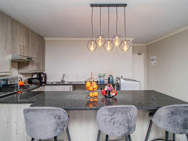 Modern kitchen featuring light wood-grain cabinetry, dark granite countertops, a breakfast bar, and contemporary pendant lighting.