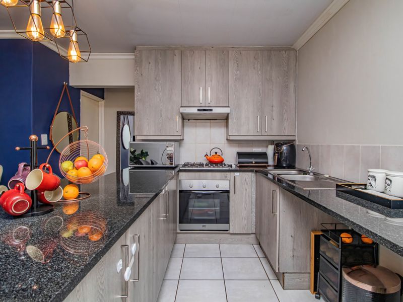 Modern kitchen featuring granite countertops, laminate cabinetry, built-in oven, gas hob, and tiled flooring in a functional U-shaped layout.