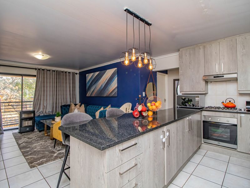 Open-plan living area featuring a modern kitchen with granite island, built-in oven, gas hob, and tiled flooring, seamlessly connected to the lounge space.
