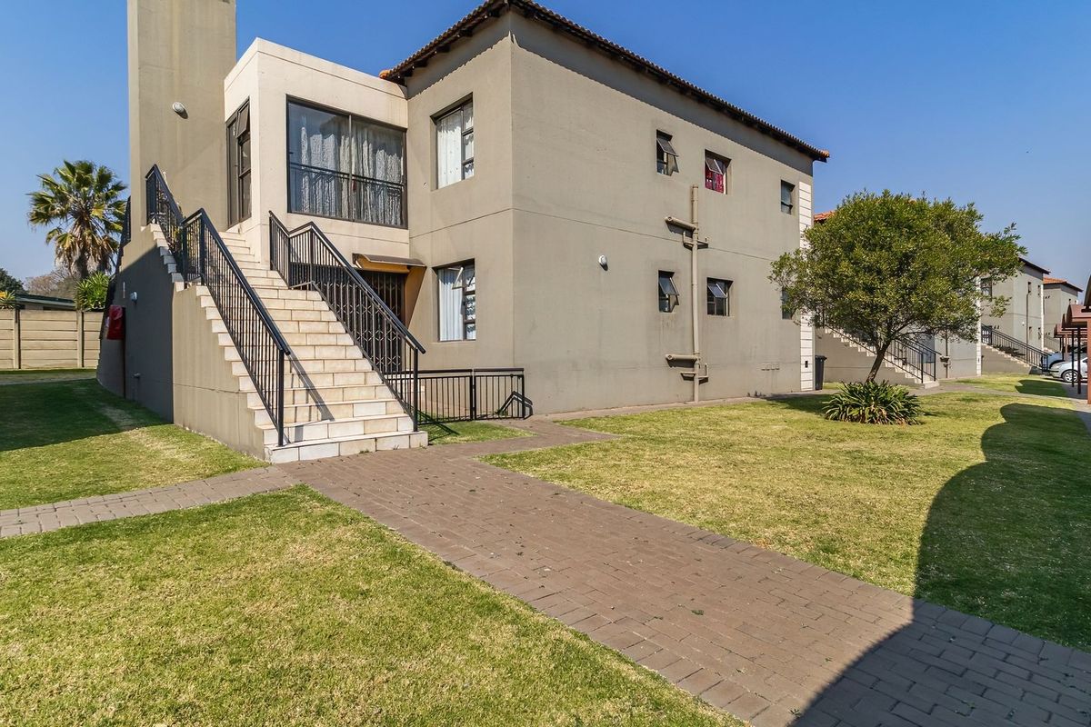 Exterior view of an apartment building featuring a paved walkway, external staircase with metal railings, and adjacent carport parking.
