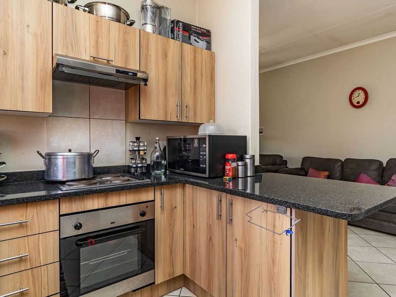 Open-plan kitchen featuring wood-look laminate cabinetry, granite countertops, and integrated appliances, flowing into the adjacent living area with tiled flooring.