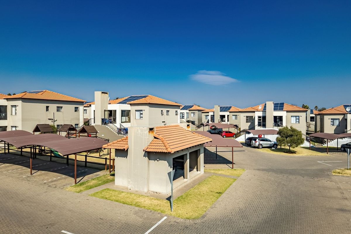 Aerial view of an apartment complex featuring multiple residential units, paved parking areas with carports, and communal facilities under a clear blue sky.
