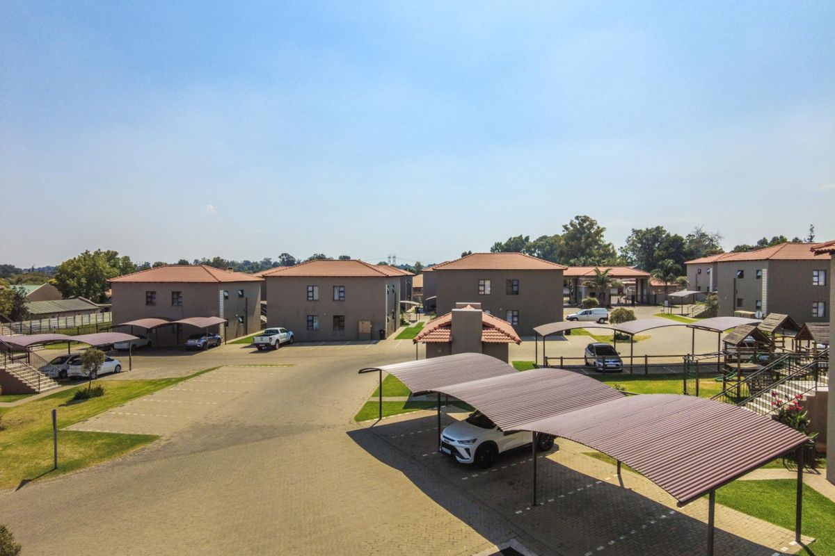Aerial view of an apartment complex featuring multiple residential buildings, paved parking areas, and covered carports within a landscaped estate.