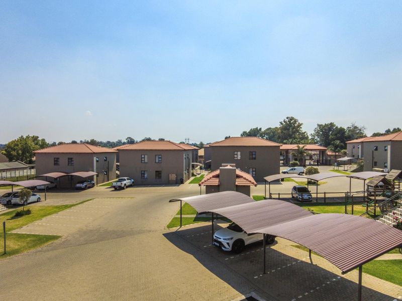 Aerial view of an apartment complex featuring multiple residential buildings, paved parking areas, and covered carports within a landscaped estate.