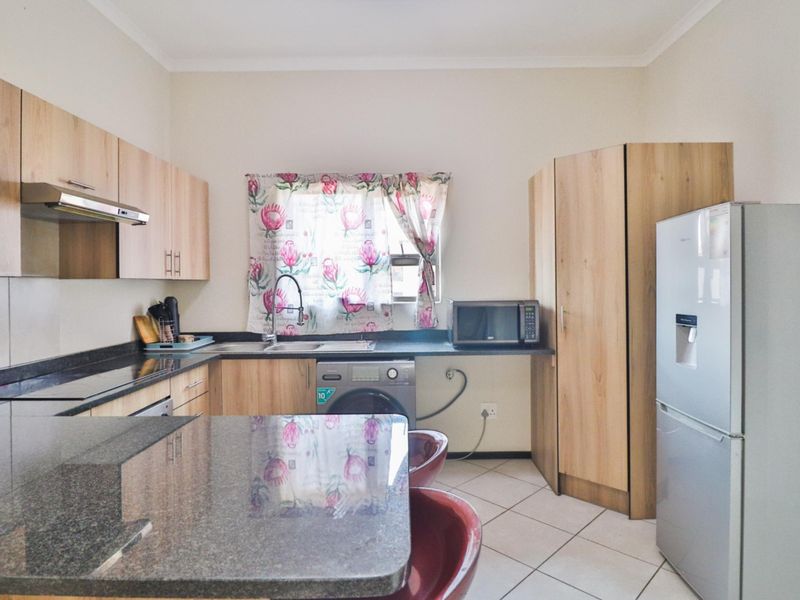 A functional kitchen featuring light wood-look cabinetry, dark granite countertops, tiled flooring, and integrated space for laundry appliances.
