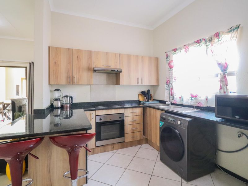 A functional kitchen featuring light wood-finish cabinetry, dark granite countertops, built-in oven and hob, and tiled flooring with an integrated laundry appliance space.