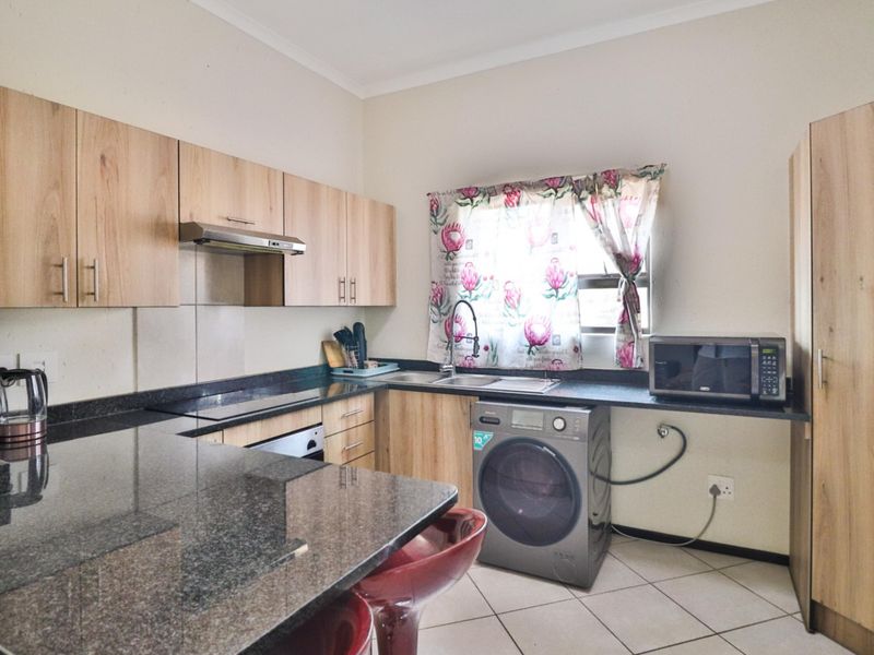 A functional kitchen featuring granite countertops, light wood cabinetry, built-in oven, extractor fan, and tiled flooring with space for a washing machine.