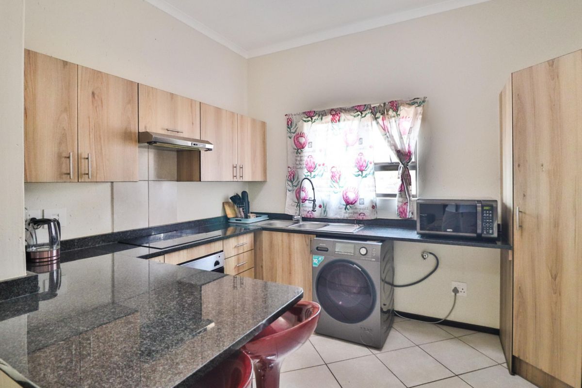 A functional kitchen featuring granite countertops, light wood cabinetry, built-in oven, extractor fan, and tiled flooring with space for a washing machine.