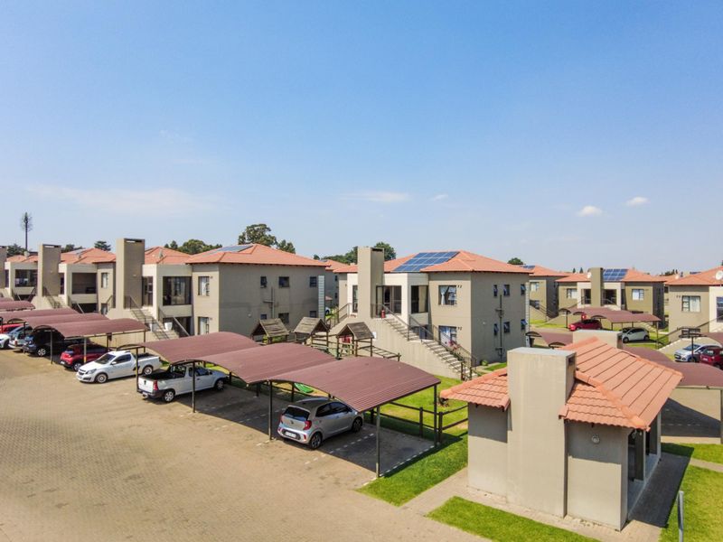 Aerial view of an apartment complex featuring multiple residential blocks, covered parking bays, and solar panel installations on tiled roofs.