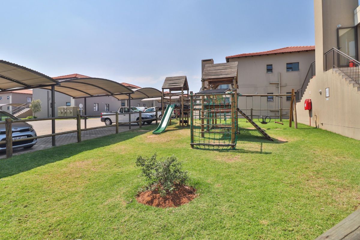 Communal outdoor area featuring a lawn, playground equipment, and covered parking bays within the apartment complex.