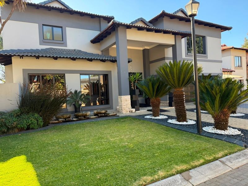 A well-maintained double-storey residential property featuring a modern facade, stone-clad pillars, a manicured front garden, and a paved driveway.