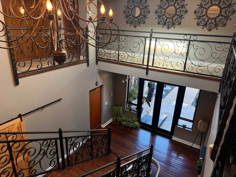 Grand double-volume entrance hall featuring a striking wrought iron staircase balustrade, rich hardwood flooring, and a large feature chandelier.