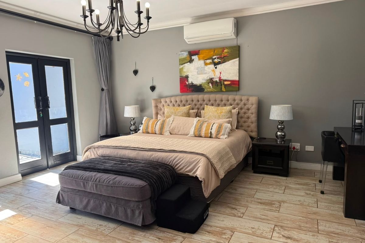 Spacious bedroom featuring tiled flooring, crown molding, a split-system air conditioner, and direct access to the outdoors via black-framed french doors.