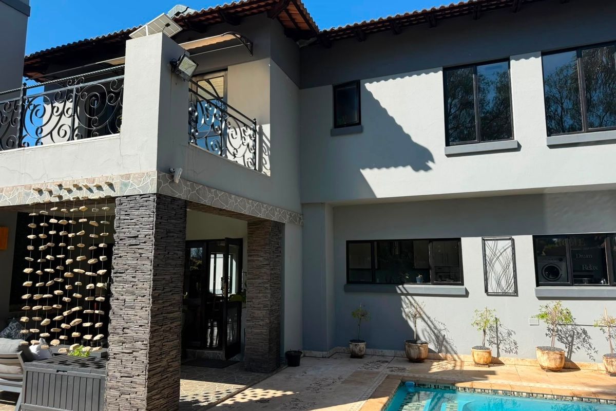 Rear elevation of a two-story house featuring a swimming pool, stone-clad pillars, and a balcony with wrought iron railings.