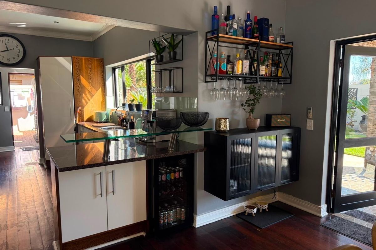 Modern kitchen area featuring a granite breakfast bar, integrated beverage fridge, and stylish wall-mounted bar storage, with direct access to the outdoor patio.