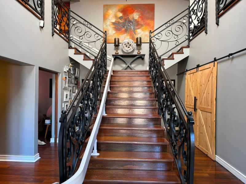 Grand entrance foyer featuring a central timber staircase with ornate wrought iron balustrades and polished hardwood flooring.