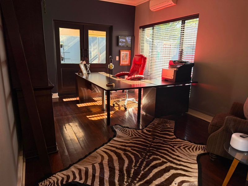 A well-lit home office featuring dark hardwood flooring, a split-system air conditioner, and direct access through french doors.