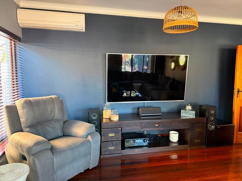 A well-maintained living room featuring dark blue accent walls, polished hardwood flooring, crown molding, and a wall-mounted split-system air conditioner.