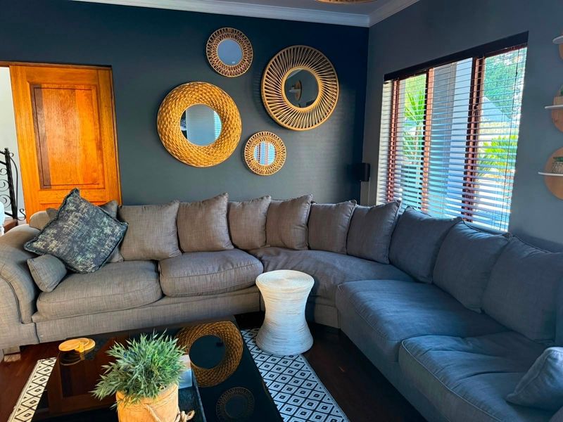 A well-maintained living room featuring dark accent walls, hardwood flooring, crown molding, and natural light filtered through wooden venetian blinds.