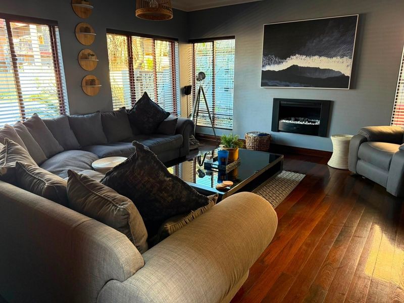 A well-maintained living room featuring rich hardwood flooring, a modern built-in fireplace, and large windows with venetian blinds.