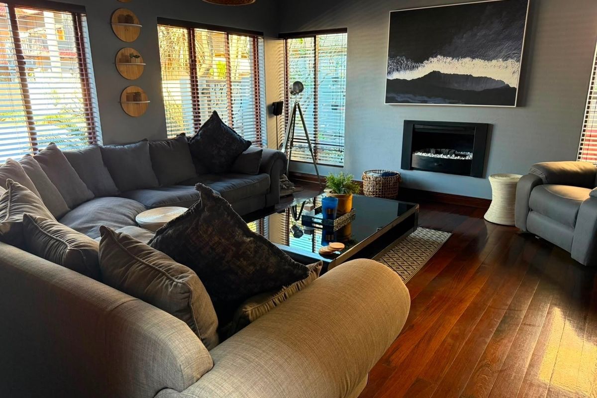 A well-maintained living room featuring rich hardwood flooring, a modern built-in fireplace, and large windows with venetian blinds.