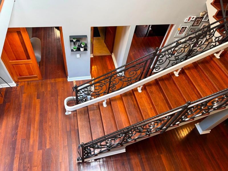 A high-angle view of a grand staircase featuring polished hardwood flooring, ornate wrought iron balustrades, and an installed stairlift.
