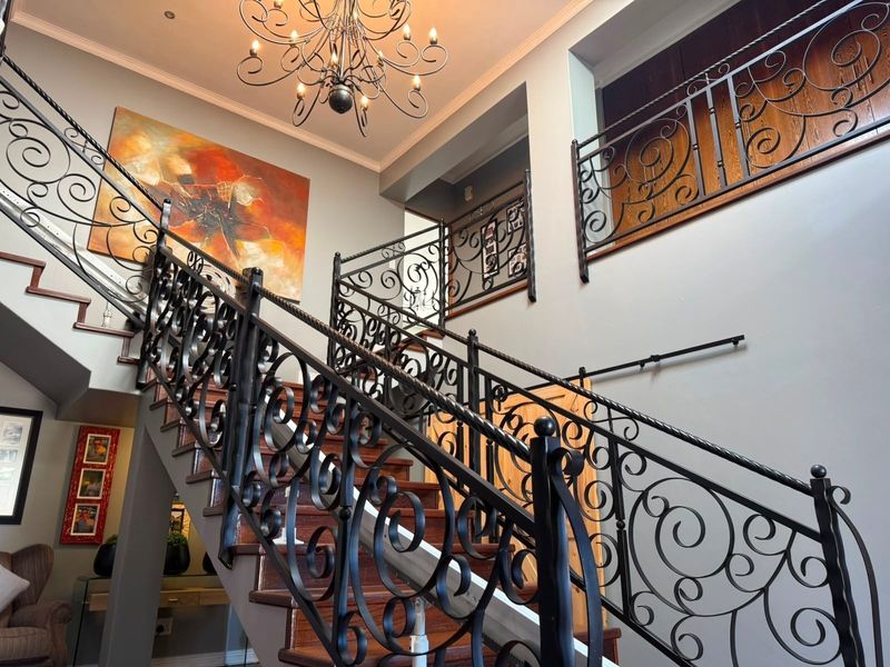 Grand entrance hall featuring a prominent wooden staircase with ornate wrought iron balustrades and a mezzanine landing.