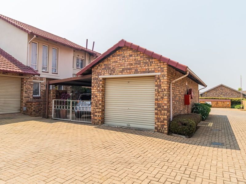 Front exterior view of a townhouse complex featuring brick facades, tiled roofs, paved driveway, and secure garage parking with an additional carport.