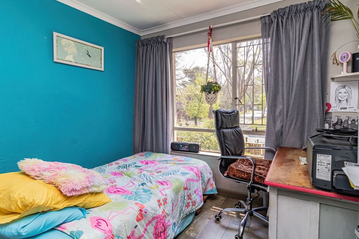 A bedroom featuring laminate flooring, a large window providing natural light, and a vibrant blue accent wall.