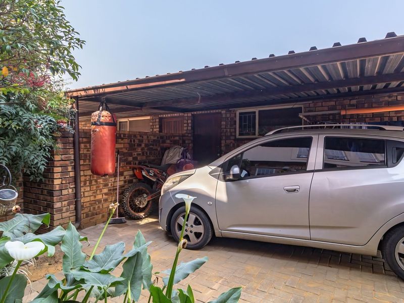 A functional outdoor carport area featuring brick wall construction and paved flooring, providing covered parking space for a vehicle.