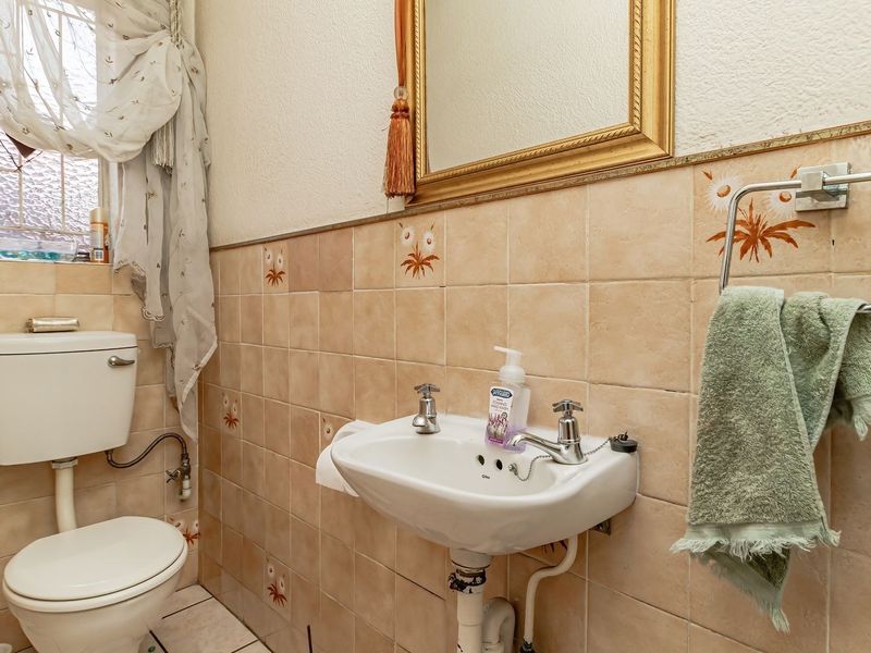 A compact guest bathroom featuring dated ceramic wall tiles, a pedestal basin, and a standard toilet.