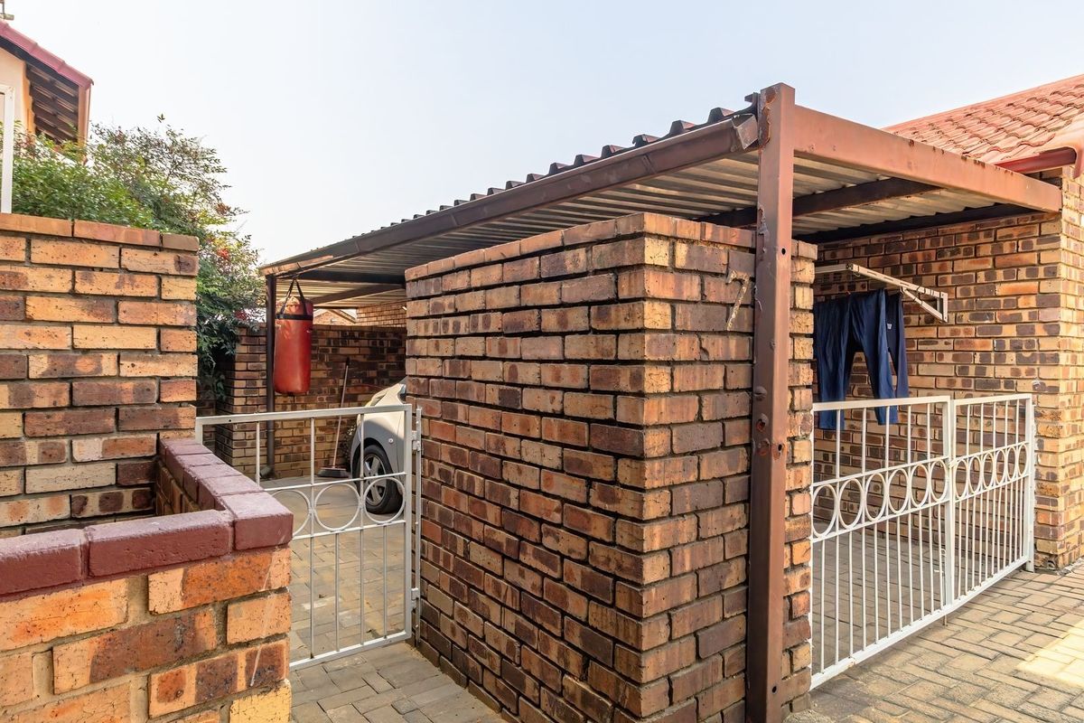 Rear exterior area featuring a brick-walled carport, paved driveway, and secure metal gate access to the property.